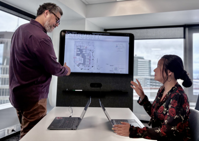 Two people at an office table discussing floor plan designs on a screen in front of them.