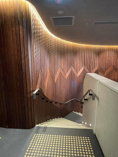 A stairway curving downwards featuring a brown korowai design on the left wall.